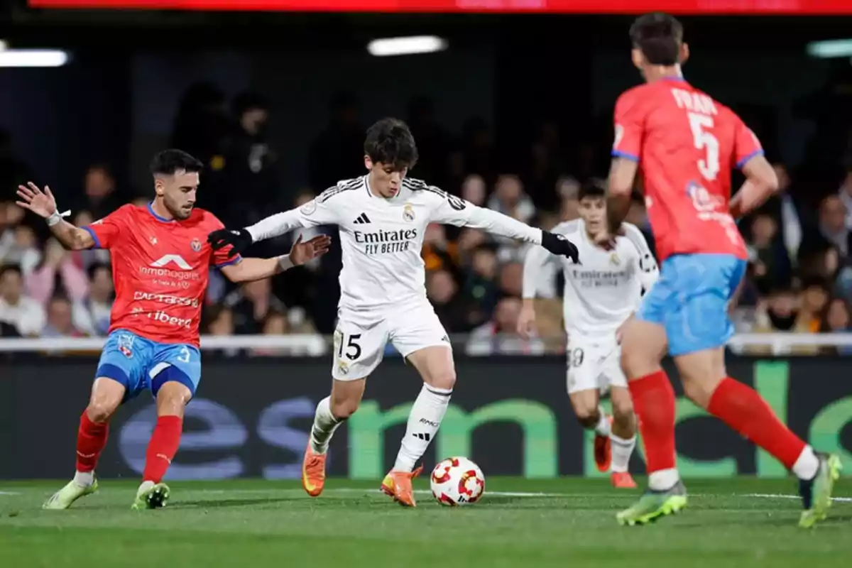 Soccer players compete for the ball in a match, one in a white uniform and the other in a red uniform. Soccer players compete for the ball in a match, one in a white uniform and the other in a red uniform.