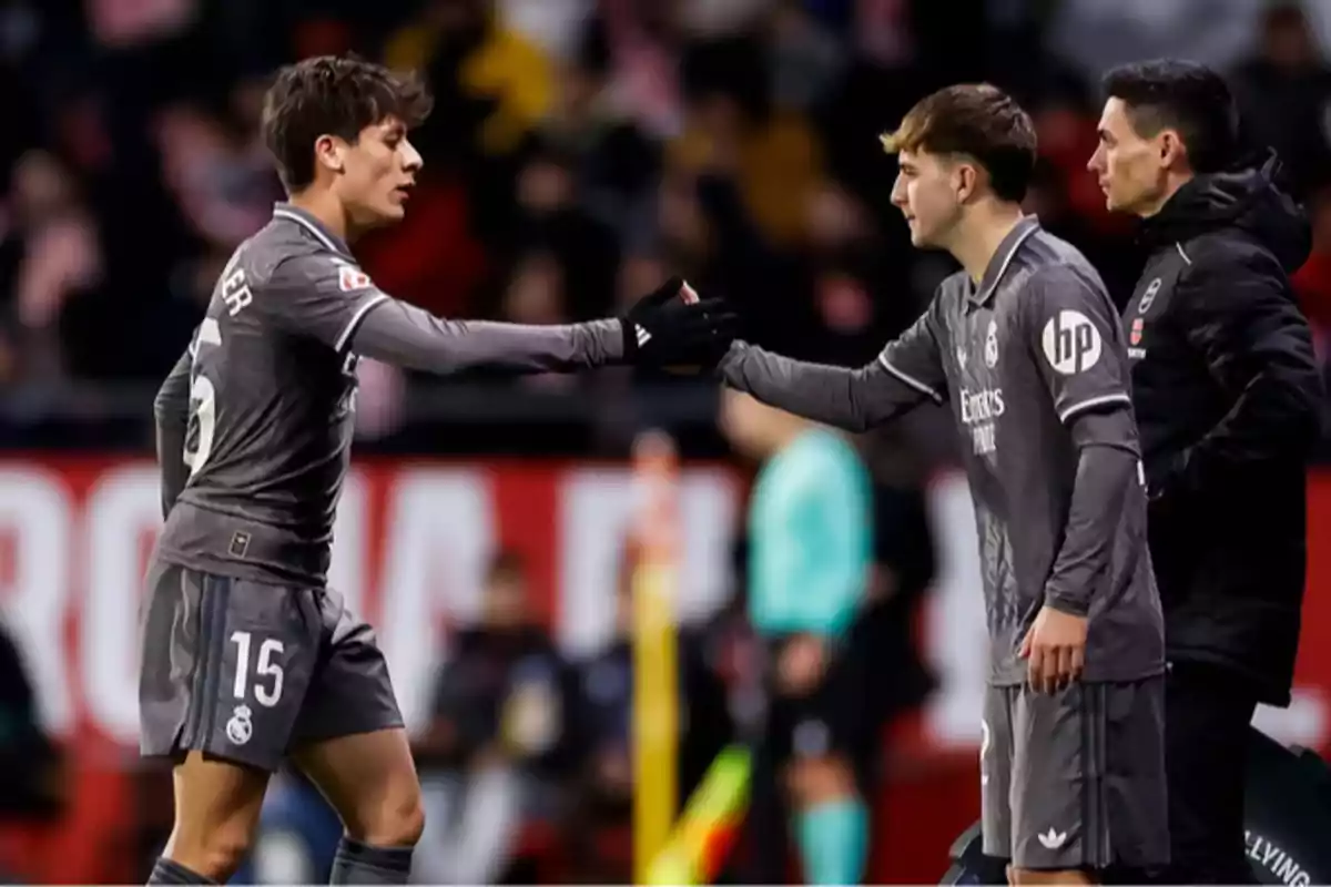 Two Real Madrid soccer players shake hands during a change of position in the match, while a member of the coaching staff looks on.