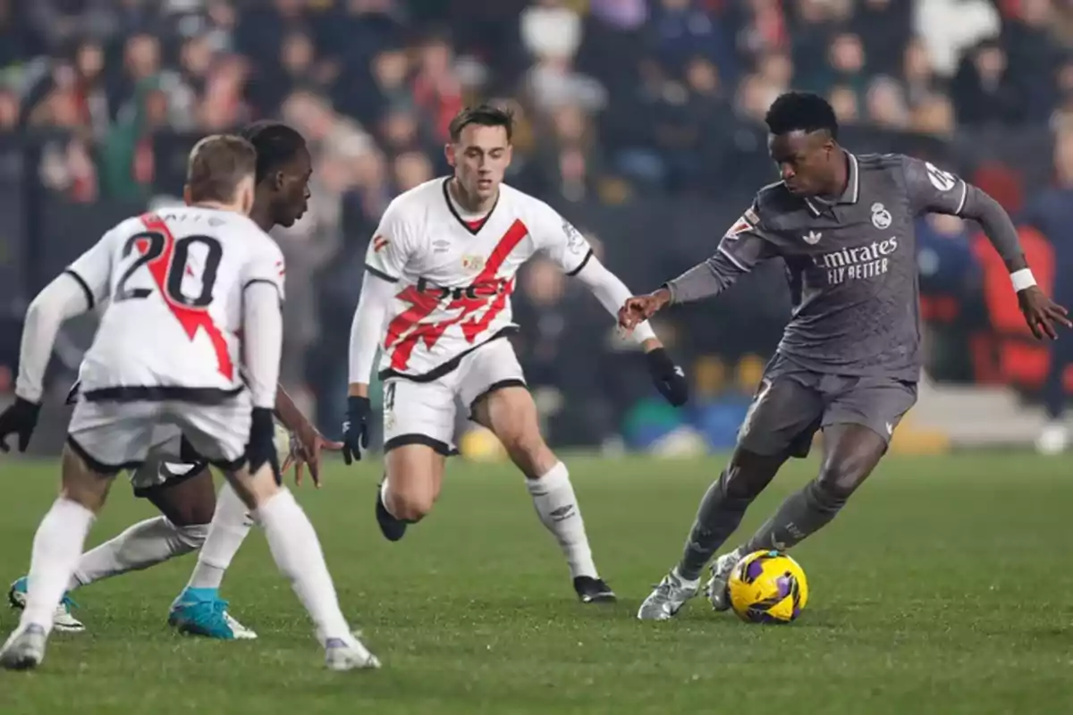 Football players in action during a match, one of them trying to advance with the ball while being surrounded by opponents.