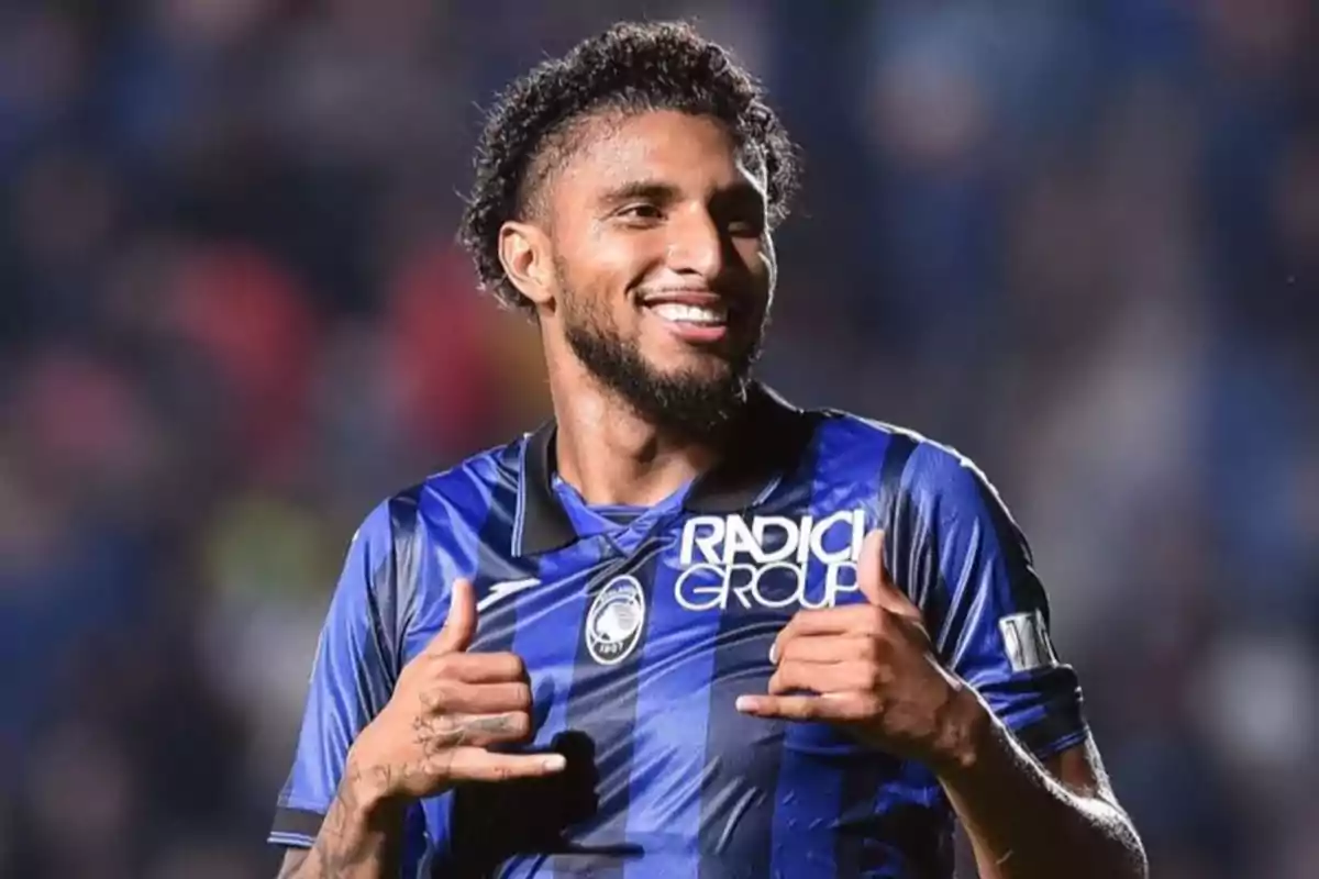 A soccer player smiles while gesturing with his hands, wearing a blue and black uniform.