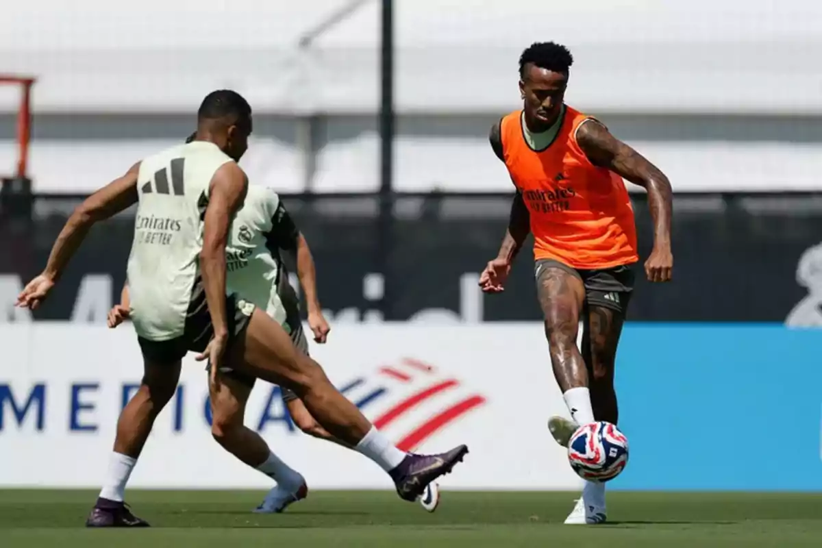 Dos futbolistas entrenan en una cancha mientras uno de ellos controla el balón y el otro intenta defender