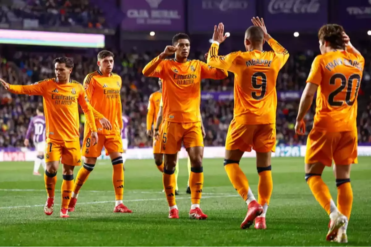 Jugadores de fútbol con uniforme naranja celebrando en el campo durante un partido.