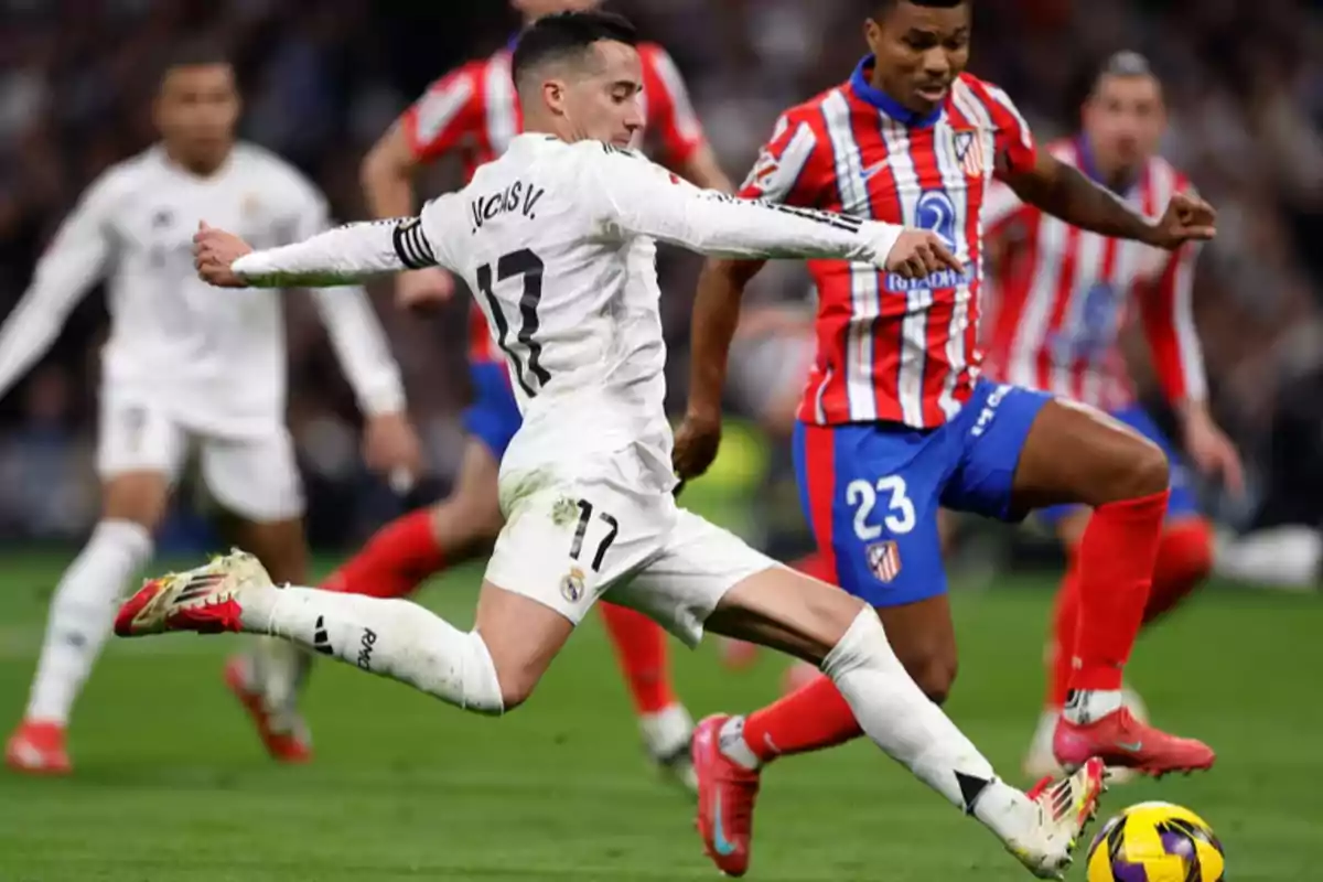 A player in a white uniform kicks the ball while a player in a red and white uniform tries to block him in a match.