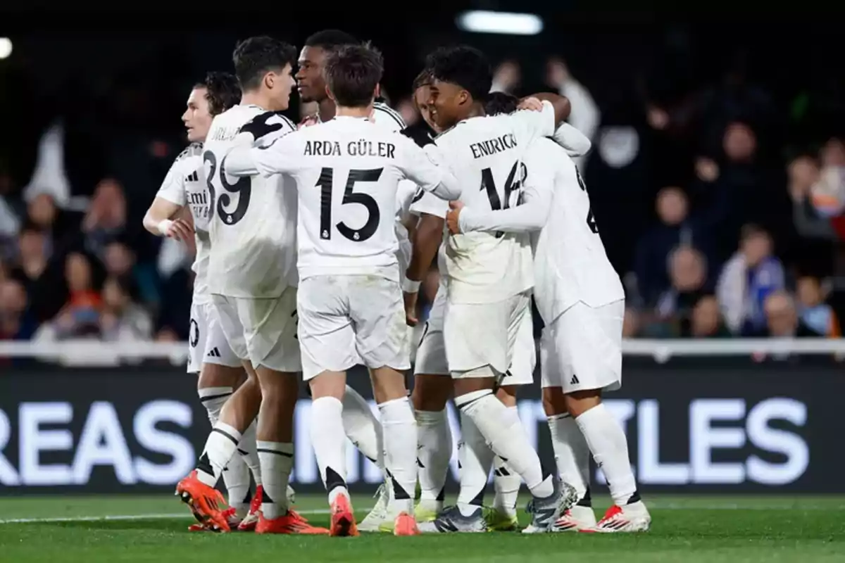 Un grupo de jugadores de fútbol con uniformes blancos se abrazan en el campo durante un partido.