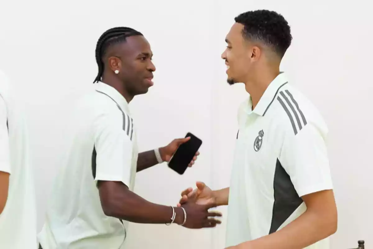 Dos jugadores del Real Madrid se saludan sonrientes mientras visten ropa deportiva blanca