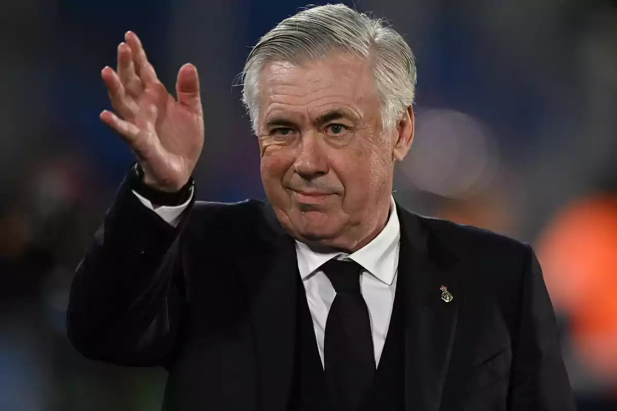 A gray-haired man in a dark suit raises his hand in a friendly gesture. A gray-haired man in a dark suit raises his hand in a friendly gesture.