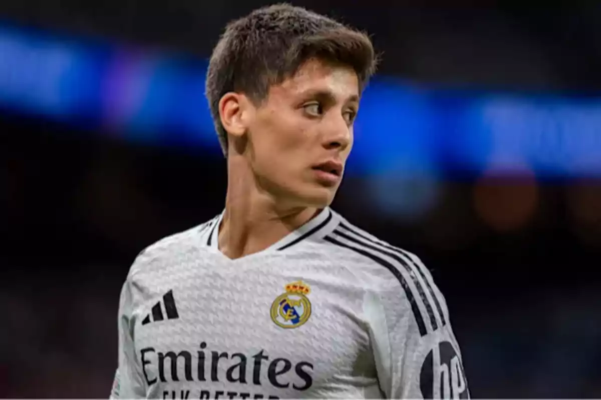 Jugador de fútbol con uniforme blanco del Real Madrid mirando hacia un lado en un estadio.