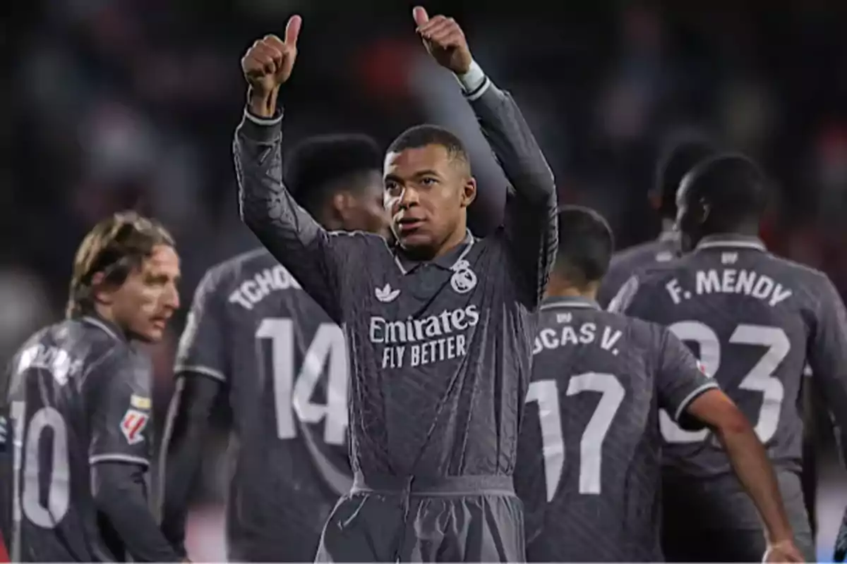 A group of soccer players in grey uniforms on the field, one of them giving a thumbs up.