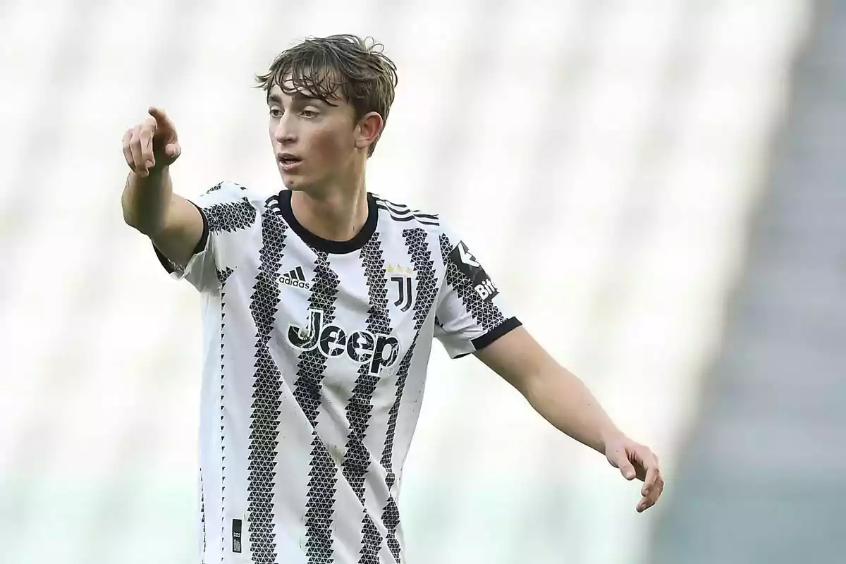 Un jugador de fútbol con el uniforme de la Juventus señala hacia adelante en un estadio.