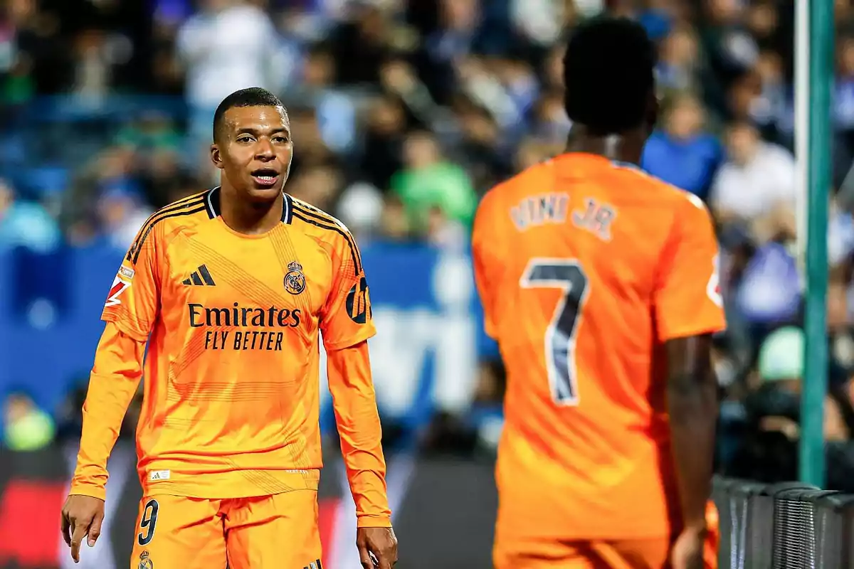 Dos jugadores de fútbol con uniformes naranjas del Real Madrid en el campo durante un partido.