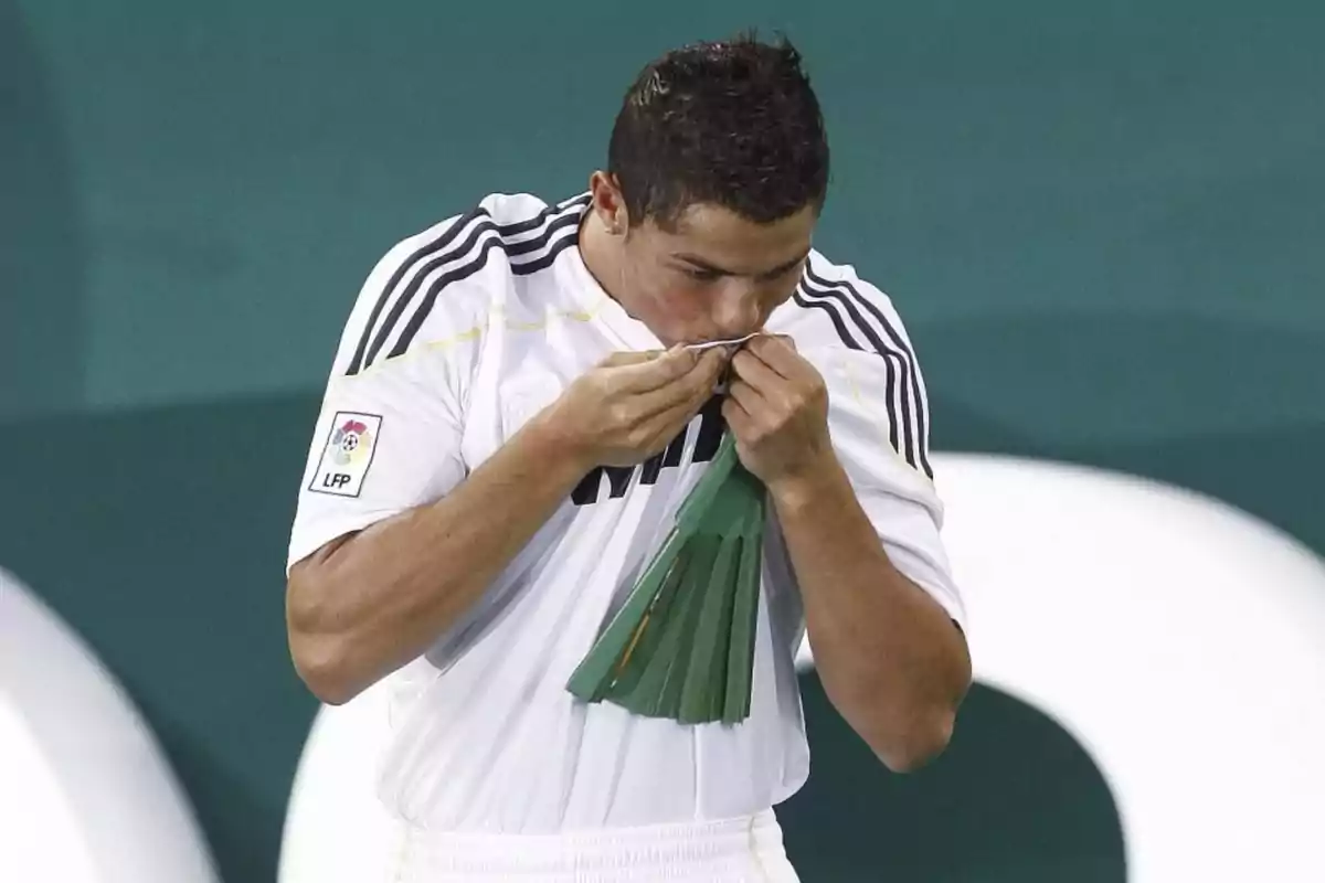Un futbolista besa el escudo de su camiseta blanca durante un partido. Un futbolista besa el escudo de su camiseta blanca durante un partido.