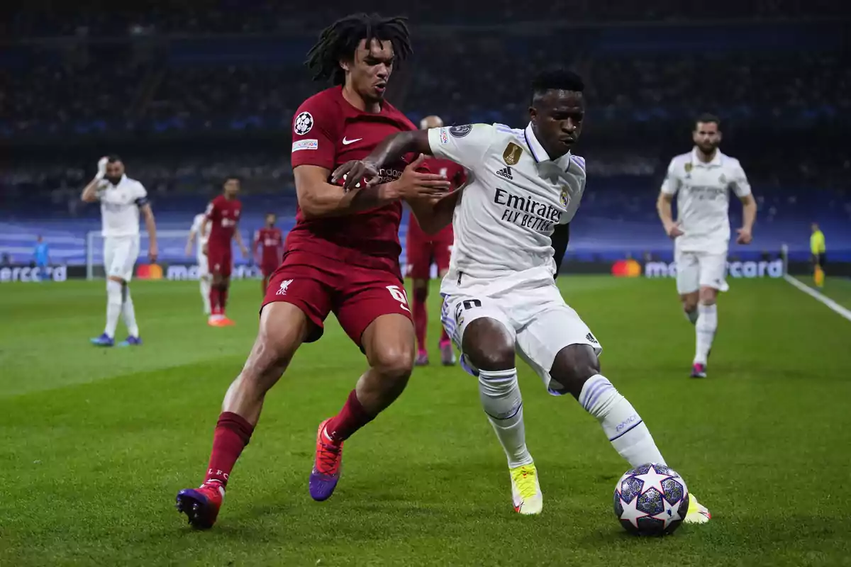 Dos futbolistas disputan el balón durante un partido entre Liverpool y Real Madrid en un estadio lleno de espectadores. Dos futbolistas disputan el balón durante un partido entre Liverpool y Real Madrid en un estadio lleno de espectadores.