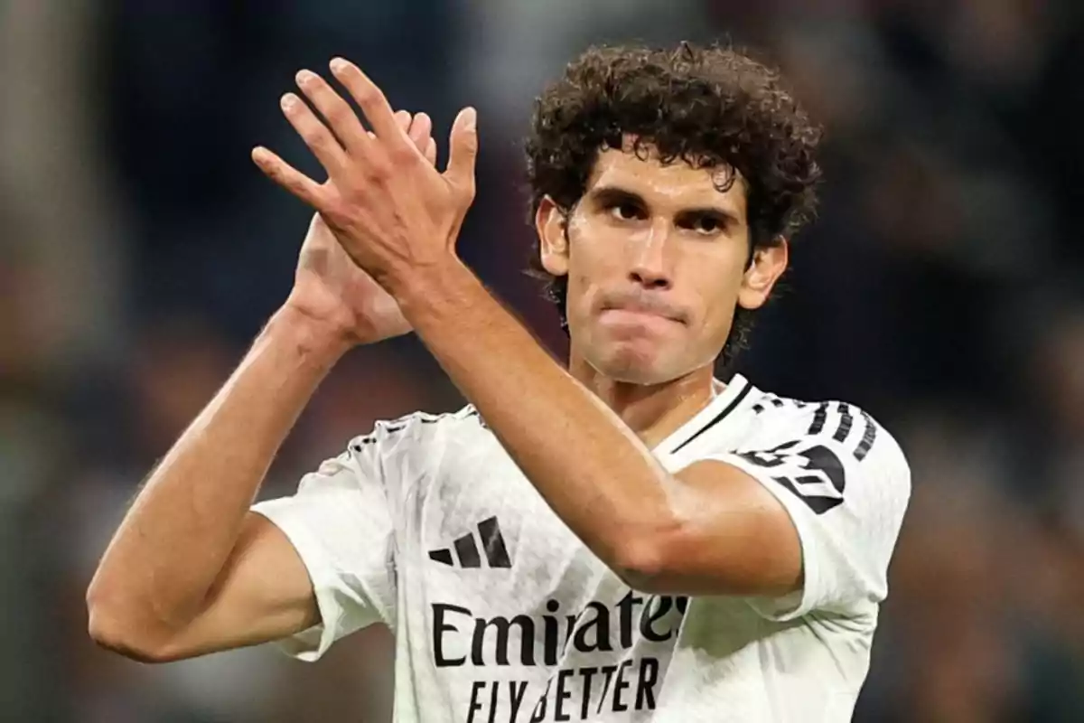 A soccer player applauding on the field in a white jersey.