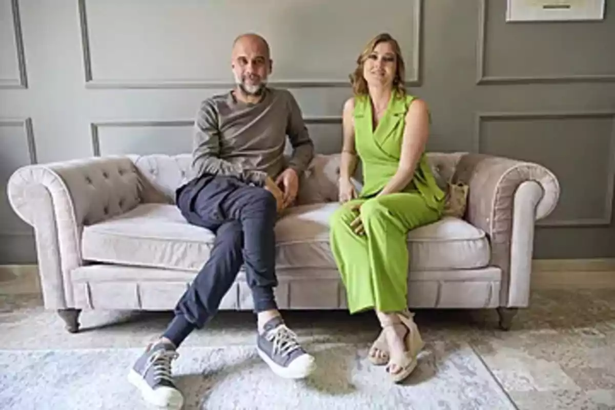 Two people sitting on a beige sofa in an elegant living room, one wearing a green outfit and the other dressed in casual dark-colored clothes. Two people sitting on a beige sofa in an elegant living room, one wearing a green outfit and the other dressed in casual dark-colored clothes.
