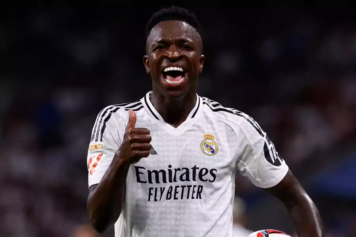 Jugador de fútbol con uniforme blanco celebrando con una sonrisa y levantando el pulgar.