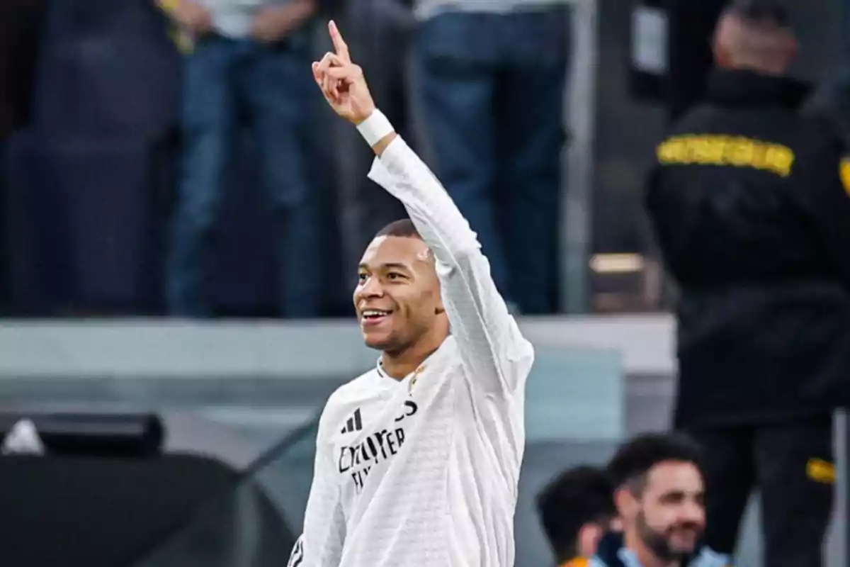 Un jugador de fútbol sonríe y levanta un dedo hacia el cielo mientras está en el campo.