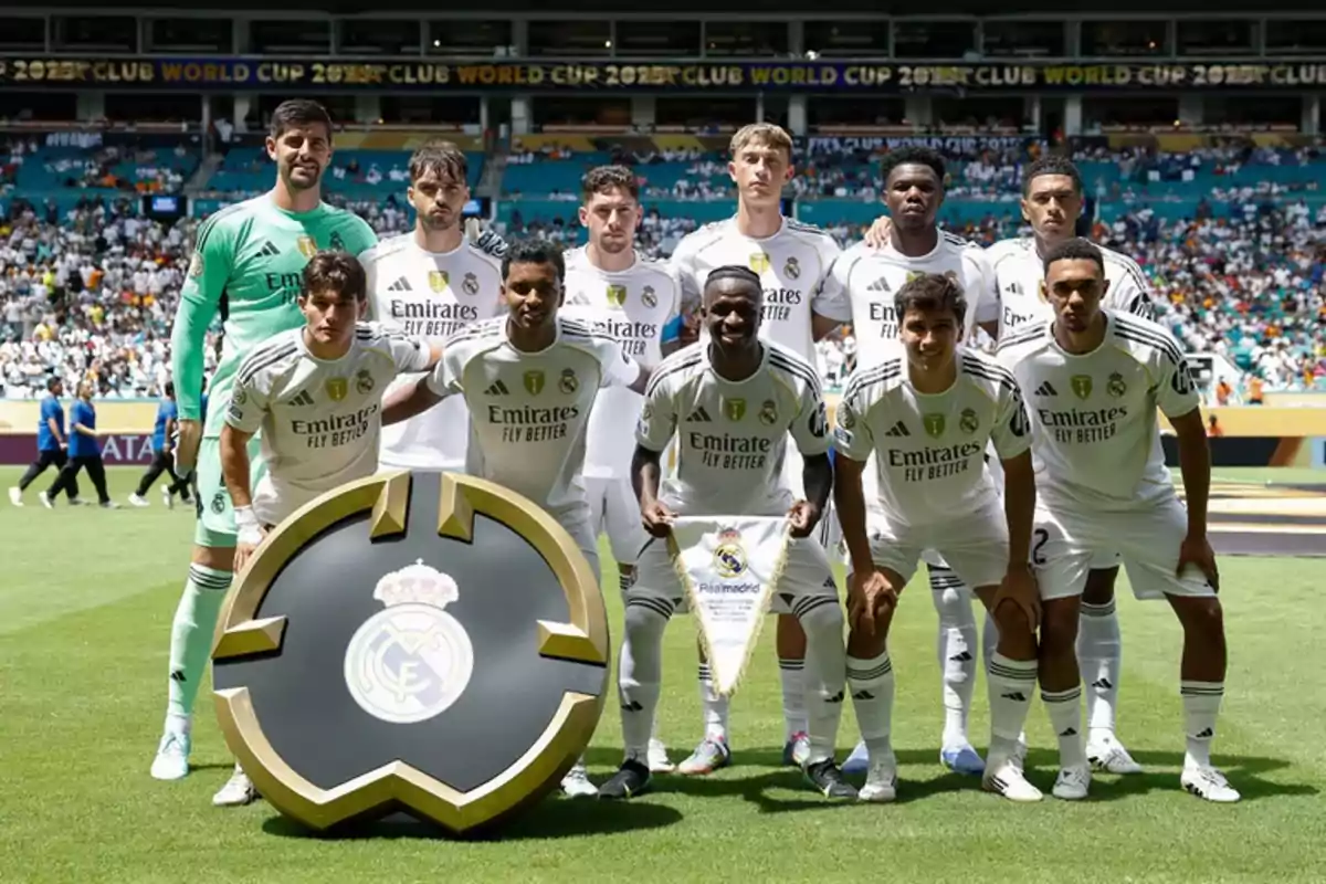 Jugadores del Real Madrid posan en el campo antes de un partido con el escudo del club al frente y el estadio lleno de aficionados al fondo Jugadores del Real Madrid posan en el campo antes de un partido con el escudo del club al frente y el estadio lleno de aficionados al fondo
