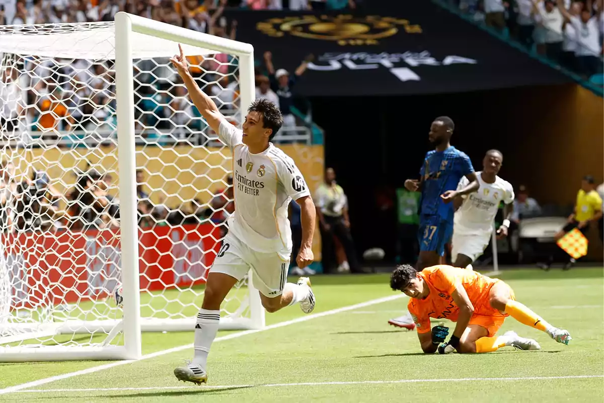 Real Madrid player celebrating a goal while the opposing goalkeeper is on the ground inside the box and the fans are cheering in the stands Real Madrid player celebrating a goal while the opposing goalkeeper is on the ground inside the box and the fans are cheering in the stands