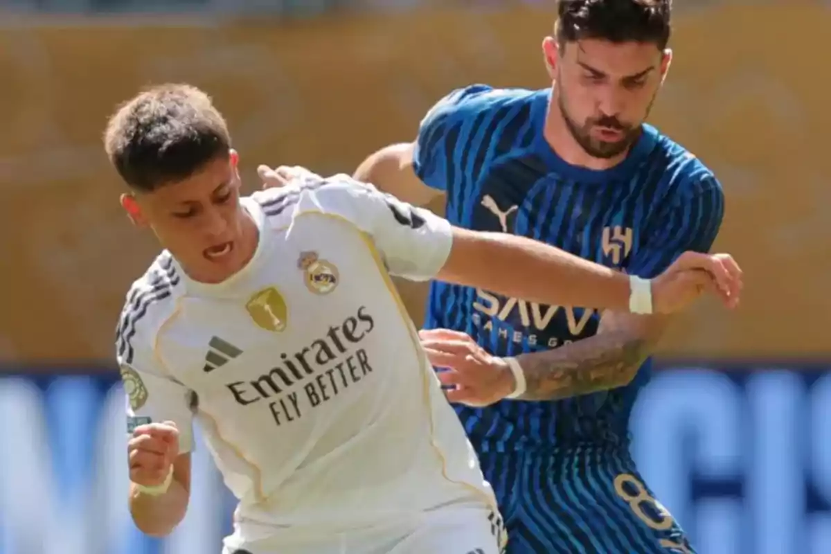 Two players compete for the ball during a match, one wearing Real Madrid's white uniform and the other wearing a blue striped uniform. Two players compete for the ball during a match, one wearing Real Madrid's white uniform and the other wearing a blue striped uniform.