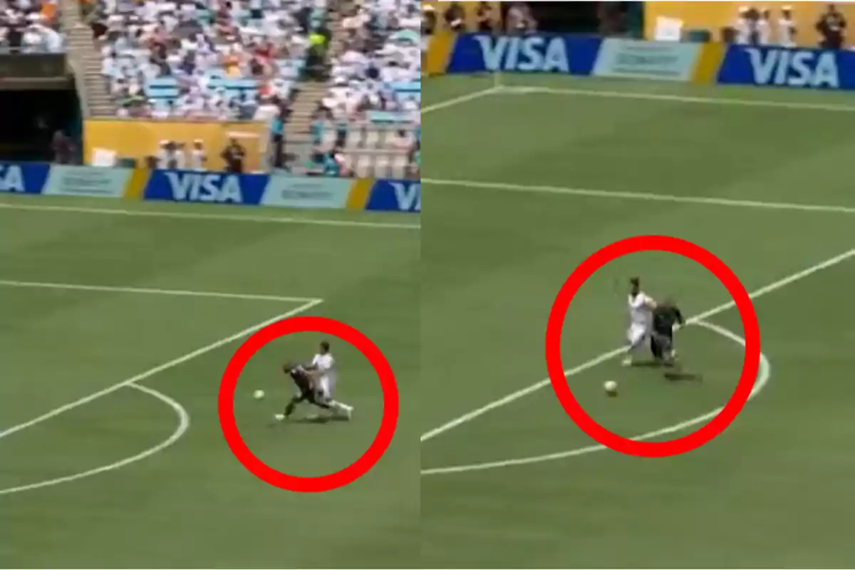 Dos jugadores de fútbol disputan el balón dentro del área mientras uno de ellos comete una falta al derribar al otro