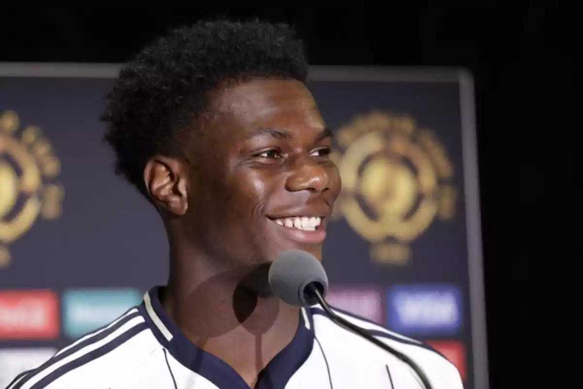 Smiling young player during a press conference with a microphone and a backdrop of sports logos