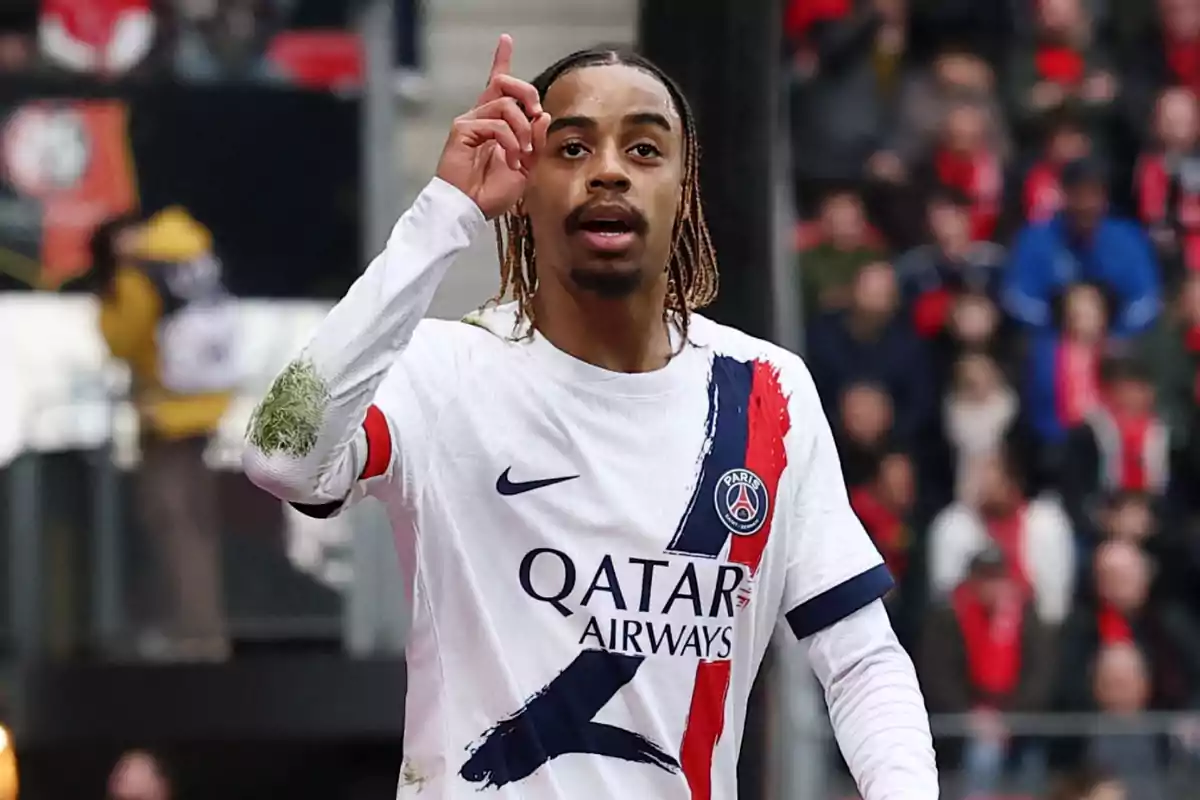 Futbolista del PSG con uniforme blanco celebrando en la cancha señalando hacia arriba con el dedo índice