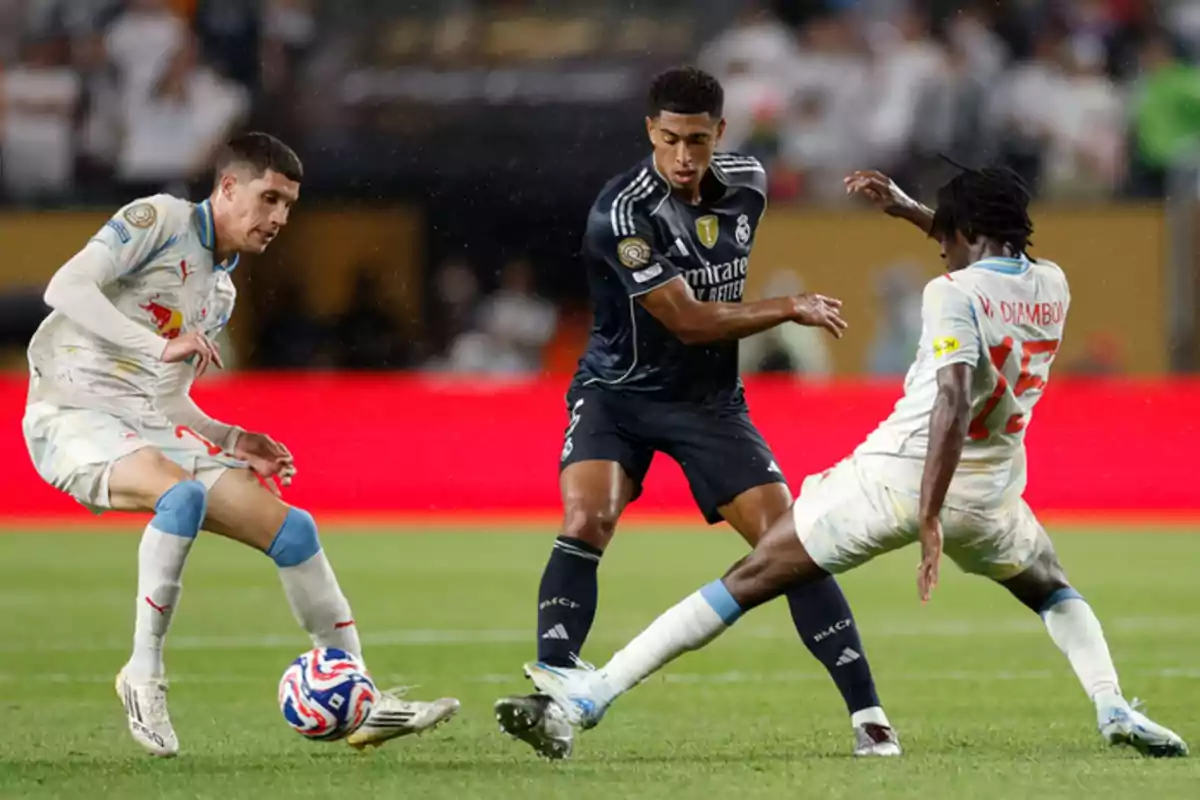 Three players compete for the ball during a match in a stadium full of spectators.