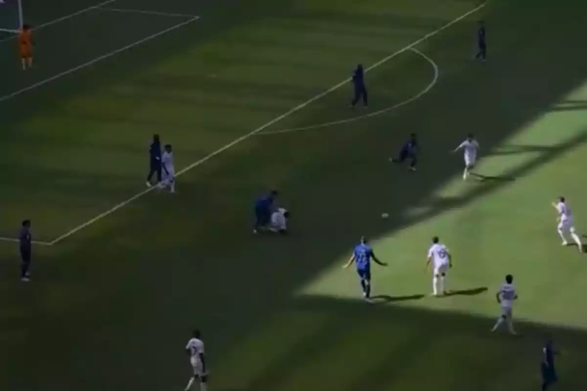 Soccer players contesting the ball near the penalty area during a match in a stadium partially lit by shadows
