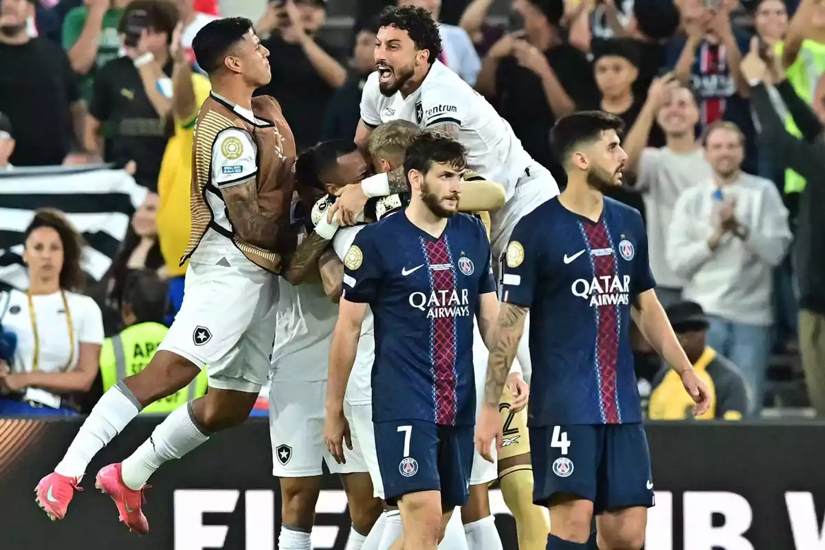 Jugadores de un equipo celebran un gol mientras los futbolistas del equipo rival caminan cabizbajos en el campo de fútbol con aficionados en las gradas al fondo Jugadores de un equipo celebran un gol mientras los futbolistas del equipo rival caminan cabizbajos en el campo de fútbol con aficionados en las gradas al fondo