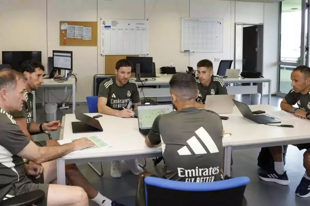 Six Real Madrid coaches sitting around a table in a meeting room while analyzing soccer tactics using laptops and sheets of paper Six Real Madrid coaches sitting around a table in a meeting room while analyzing soccer tactics using laptops and sheets of paper