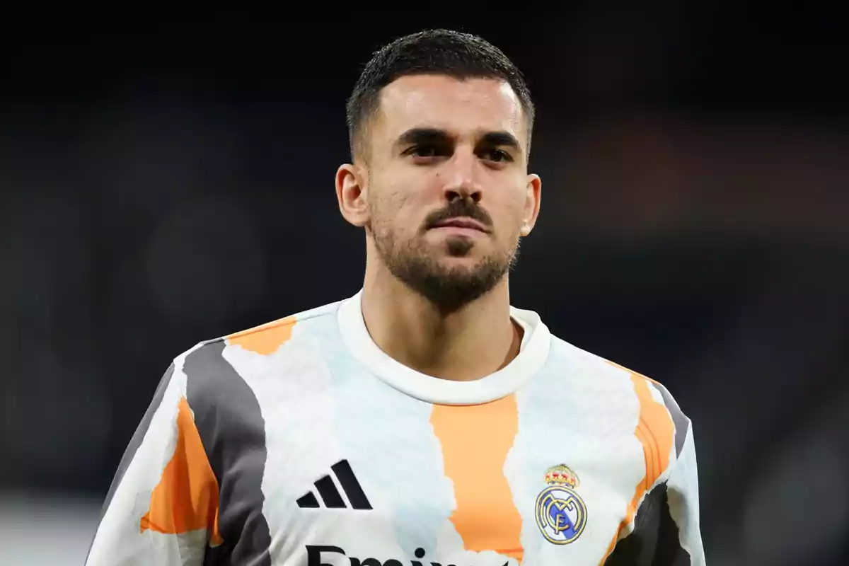 Futbolista con barba y cabello corto vistiendo una camiseta de entrenamiento del Real Madrid con colores blanco, naranja y gris