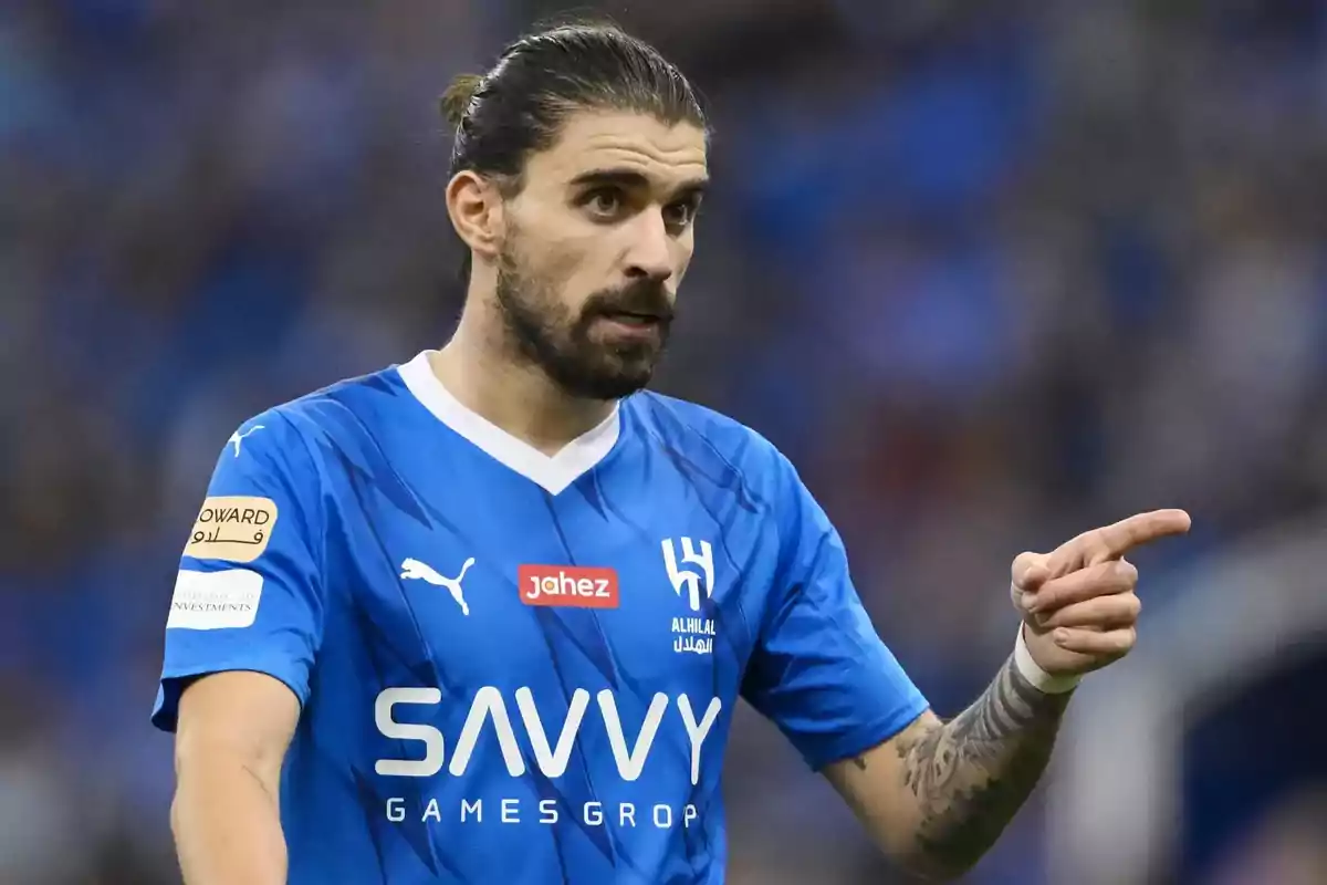 Futbolista con barba y cabello recogido viste uniforme azul y señala con el dedo durante un partido Futbolista con barba y cabello recogido viste uniforme azul y señala con el dedo durante un partido