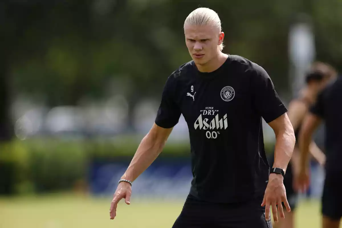 Blond player wearing a black Manchester City training jersey on a grass field Blond player wearing a black Manchester City training jersey on a grass field