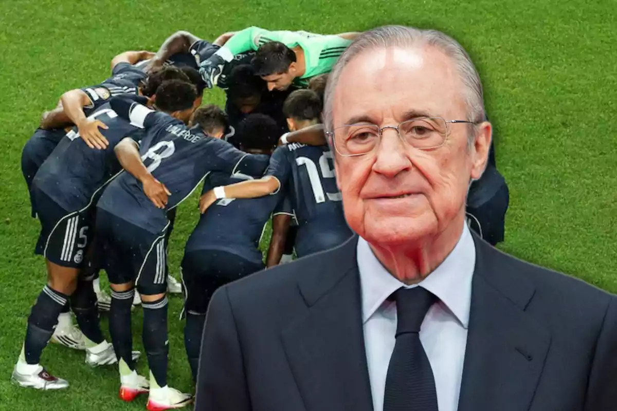 Un grupo de futbolistas con uniforme oscuro se abrazan en círculo sobre el césped mientras un hombre mayor con gafas y traje aparece en primer plano