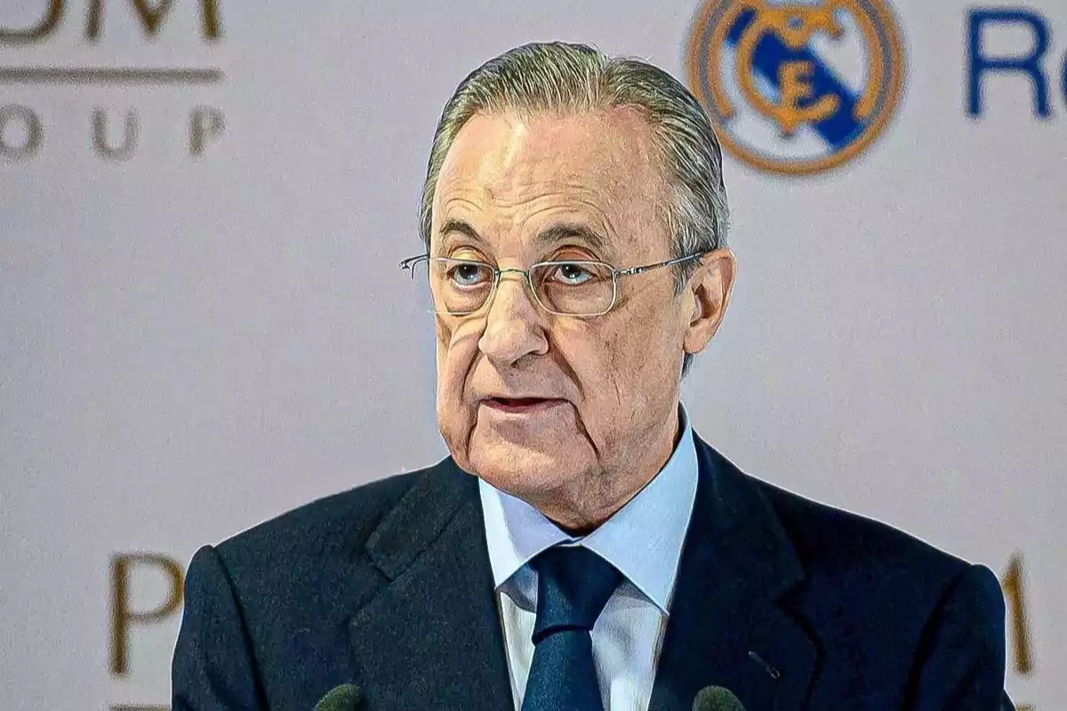 Gray-haired man with glasses speaking in front of a microphone with a background featuring a sports logo. Gray-haired man with glasses speaking in front of a microphone with a background featuring a sports logo.