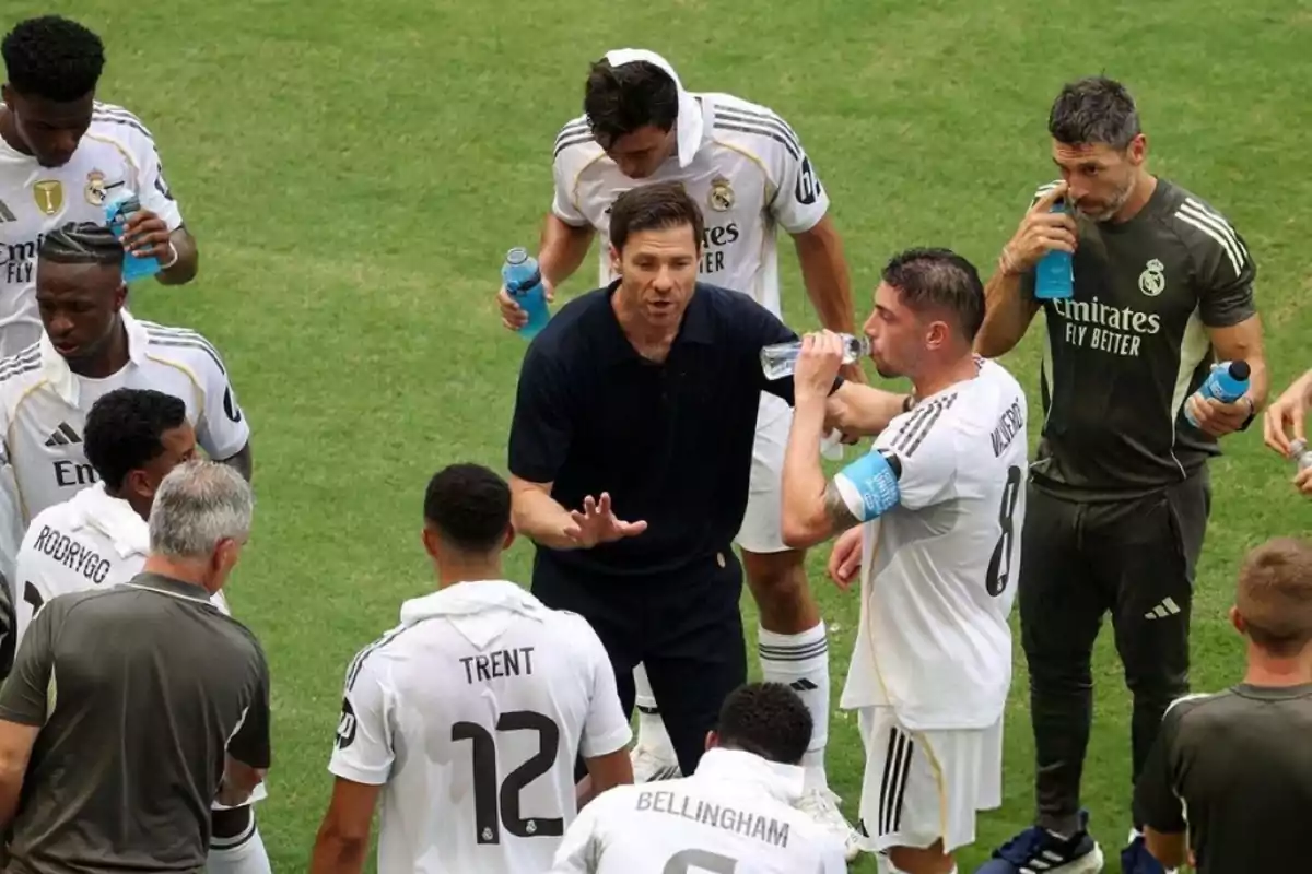 Un entrenador de fútbol da indicaciones a sus jugadores durante una pausa en el partido mientras algunos futbolistas beben agua y otros escuchan atentamente en el campo de juego Un entrenador de fútbol da indicaciones a sus jugadores durante una pausa en el partido mientras algunos futbolistas beben agua y otros escuchan atentamente en el campo de juego