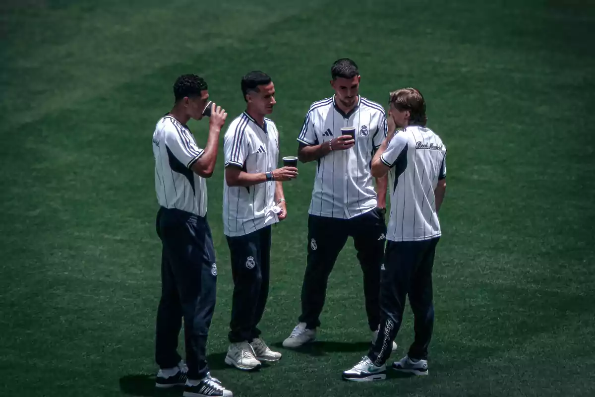 Cuatro futbolistas con uniforme de entrenamiento del Real Madrid conversan y beben de vasos en un campo de césped Cuatro futbolistas con uniforme de entrenamiento del Real Madrid conversan y beben de vasos en un campo de césped