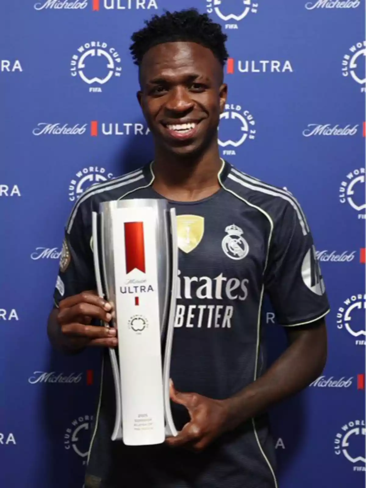 Real Madrid player smiles while holding a trophy in front of a blue background with Club World Cup and Michelob Ultra logos