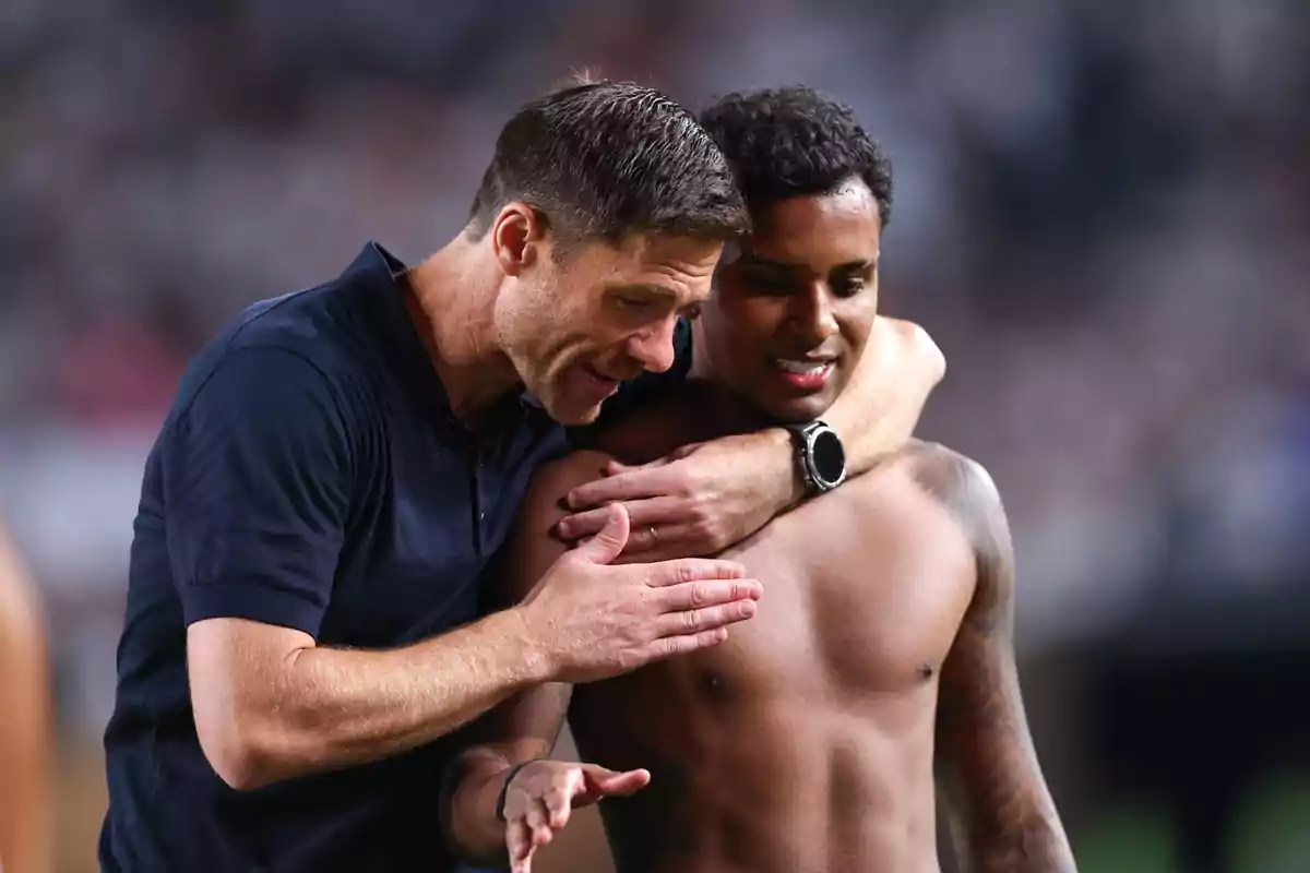 Un entrenador abraza y motiva a un jugador sin camiseta en un estadio de fútbol