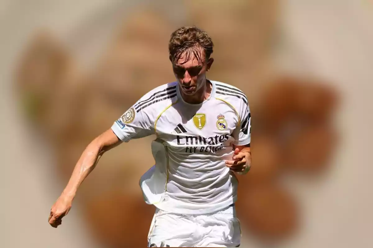 Futbolista con uniforme blanco del Real Madrid corriendo en el campo con fondo desenfocado.