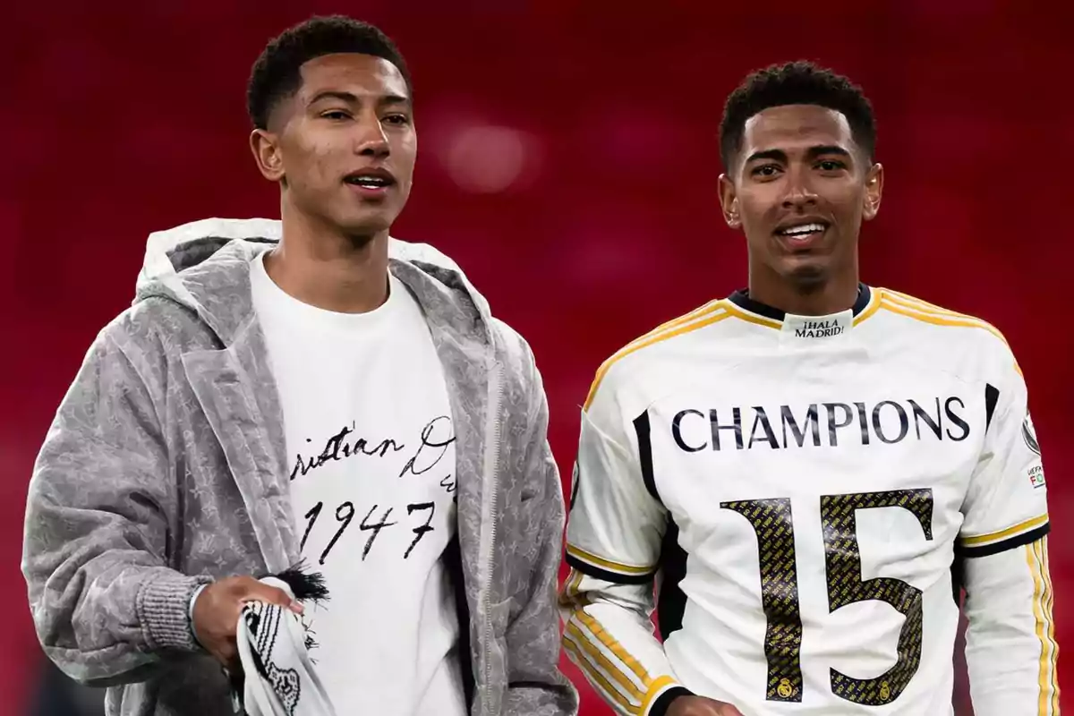 Dos jóvenes sonríen frente a un fondo rojo, uno lleva una camiseta blanca con chaqueta gris y el otro una camiseta de fútbol blanca con la palabra Champions y el número 15