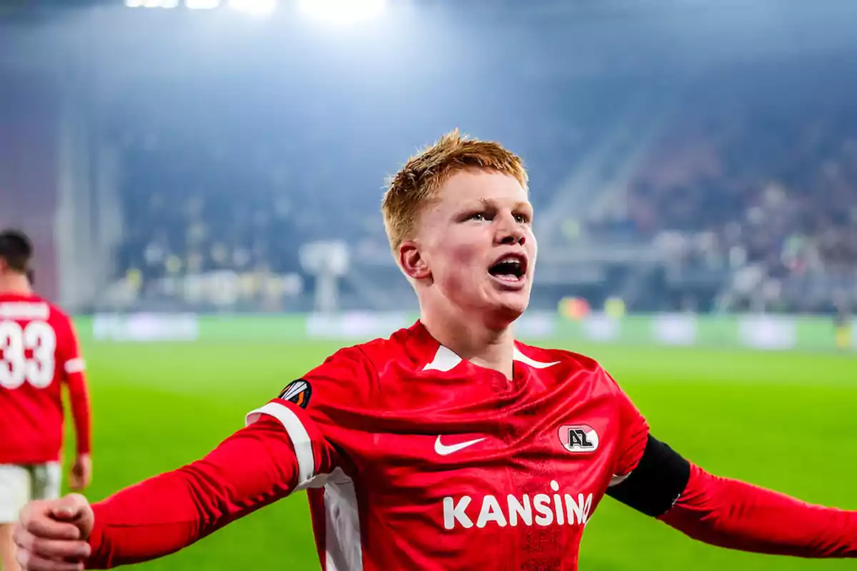 Soccer player celebrating on the field with arms outstretched, wearing a red AZ Alkmaar uniform Soccer player celebrating on the field with arms outstretched, wearing a red AZ Alkmaar uniform