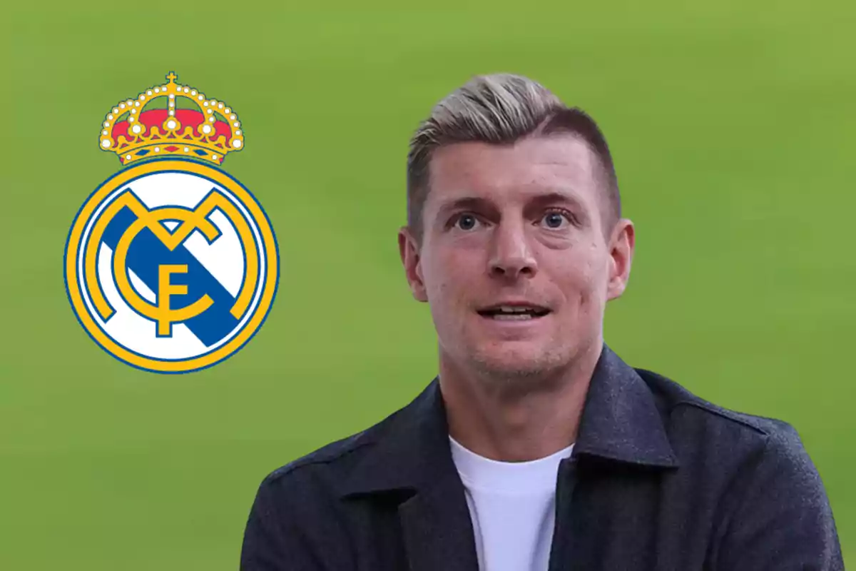 Blond man with a dark jacket and white t-jersey in front of a green background next to the Real Madrid crest