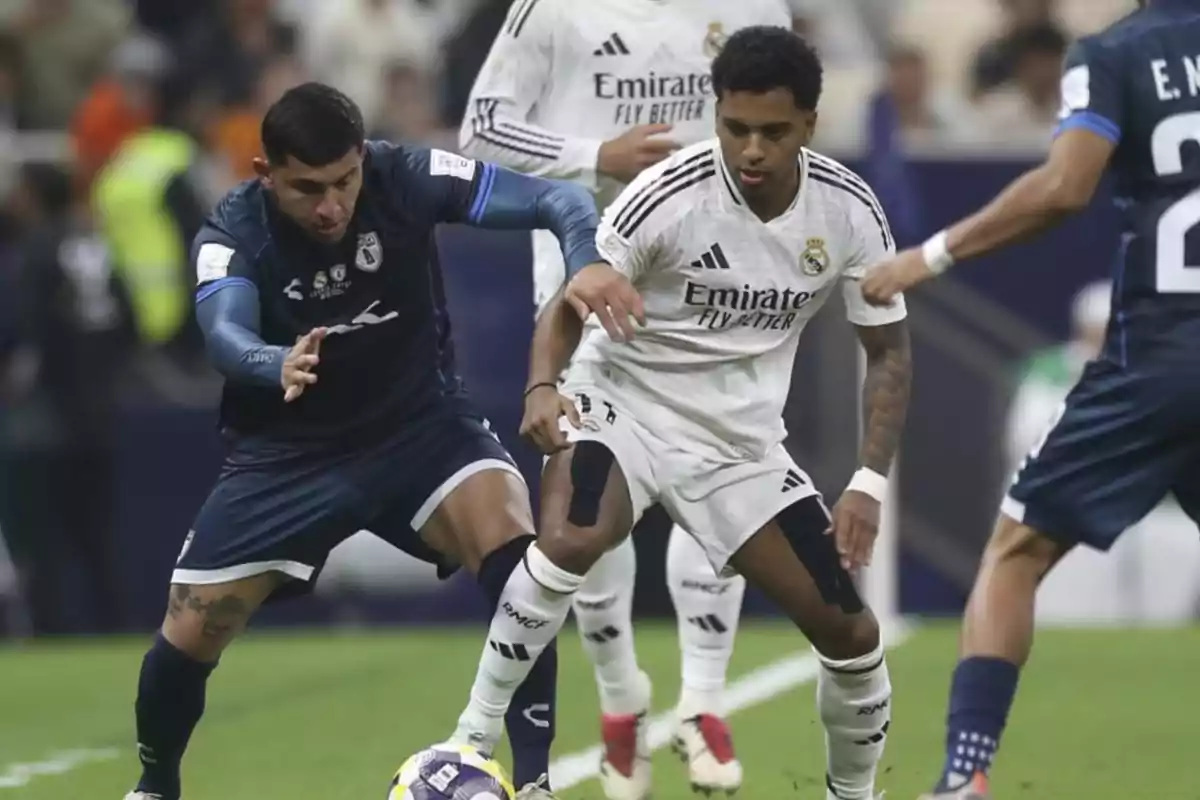 Two players compete for the ball during a match between a team in white uniforms and another in navy blue uniforms. Two players compete for the ball during a match between a team in white uniforms and another in navy blue uniforms.