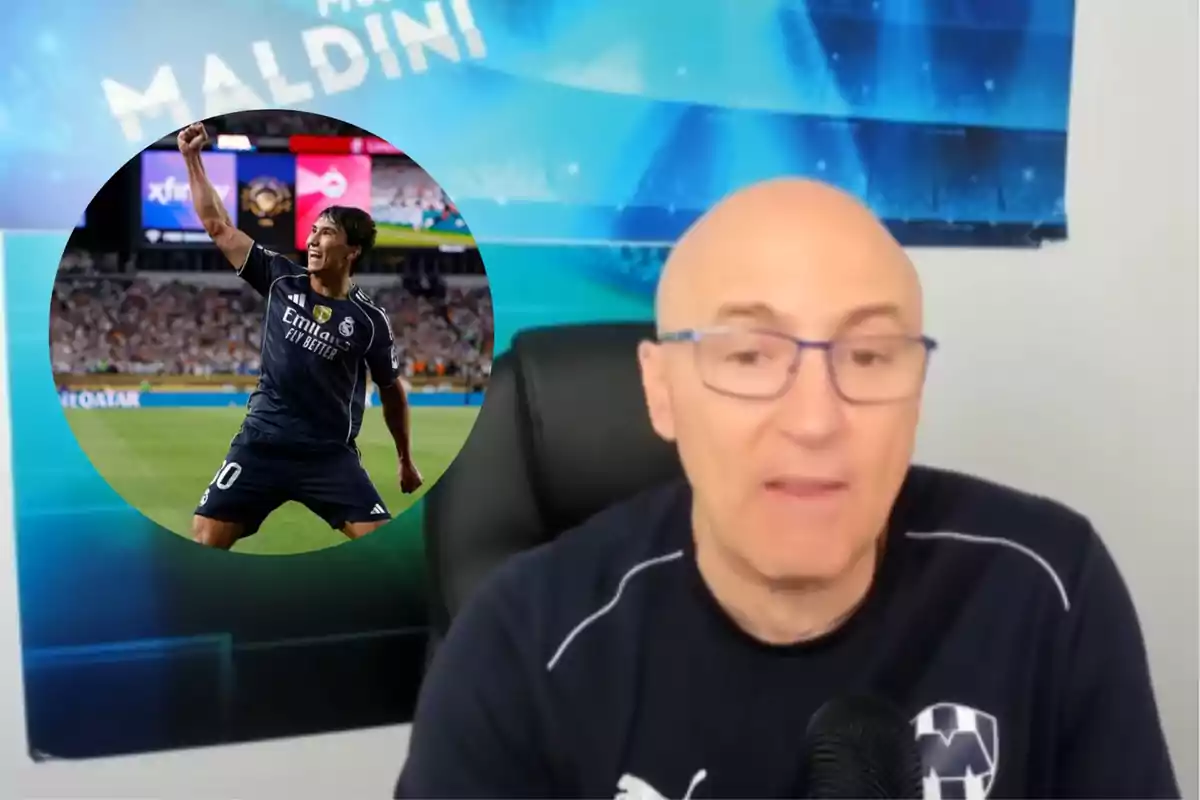 Hombre calvo con gafas y camiseta azul oscuro hablando frente a un micrófono con un fondo azul que dice Maldini y un círculo con un futbolista celebrando en un estadio lleno