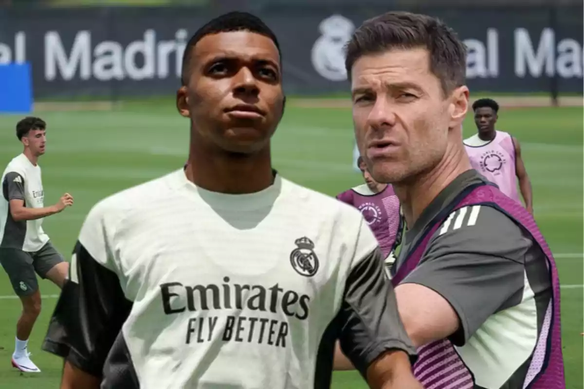 Dos personas en primer plano con uniforme de entrenamiento del Real Madrid en un campo de fútbol, al fondo otros jugadores entrenando.
