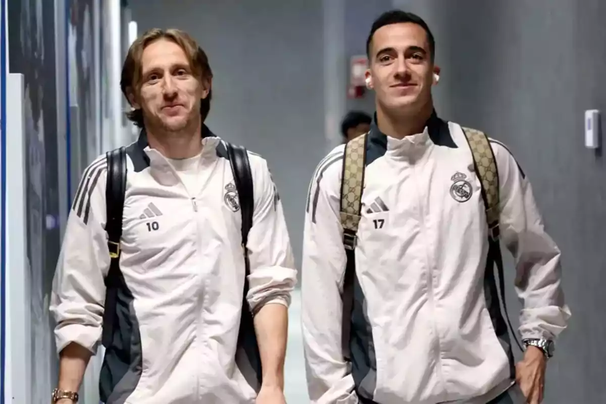 Dos futbolistas del Real Madrid caminando por un pasillo con chaquetas deportivas blancas y mochilas Dos futbolistas del Real Madrid caminando por un pasillo con chaquetas deportivas blancas y mochilas