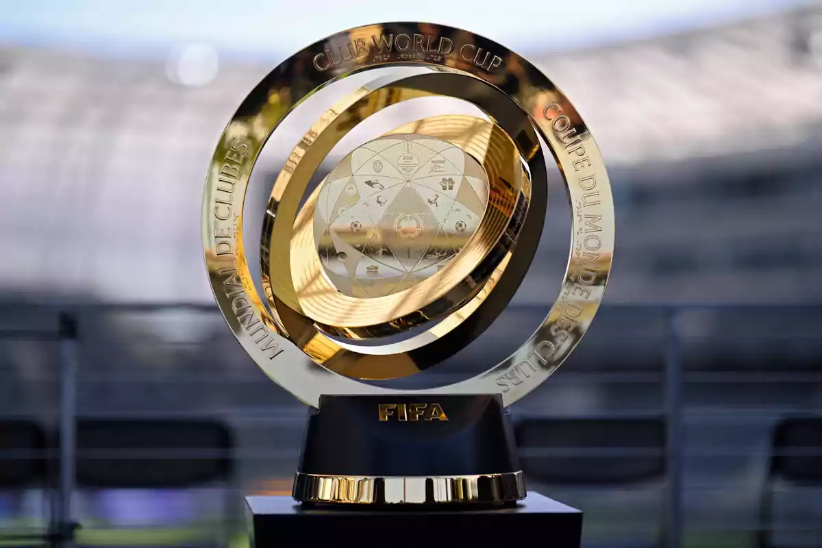 Trofeo dorado del Mundial de Clubes de la FIFA sobre una base negra con letras doradas y un estadio desenfocado al fondo