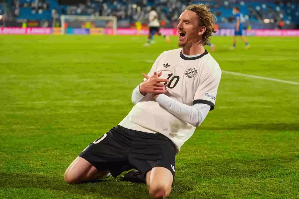 Soccer player celebrating a goal kneeling on the grass with a joyful expression and arms crossed, pretending to make pistols with his hands. Soccer player celebrating a goal kneeling on the grass with a joyful expression and arms crossed, pretending to make pistols with his hands.
