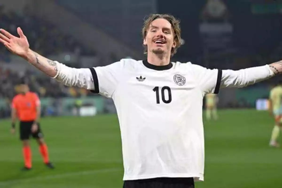 Futbolista celebrando con los brazos abiertos en un estadio durante un partido, lleva puesta una camiseta blanca con el número 10.